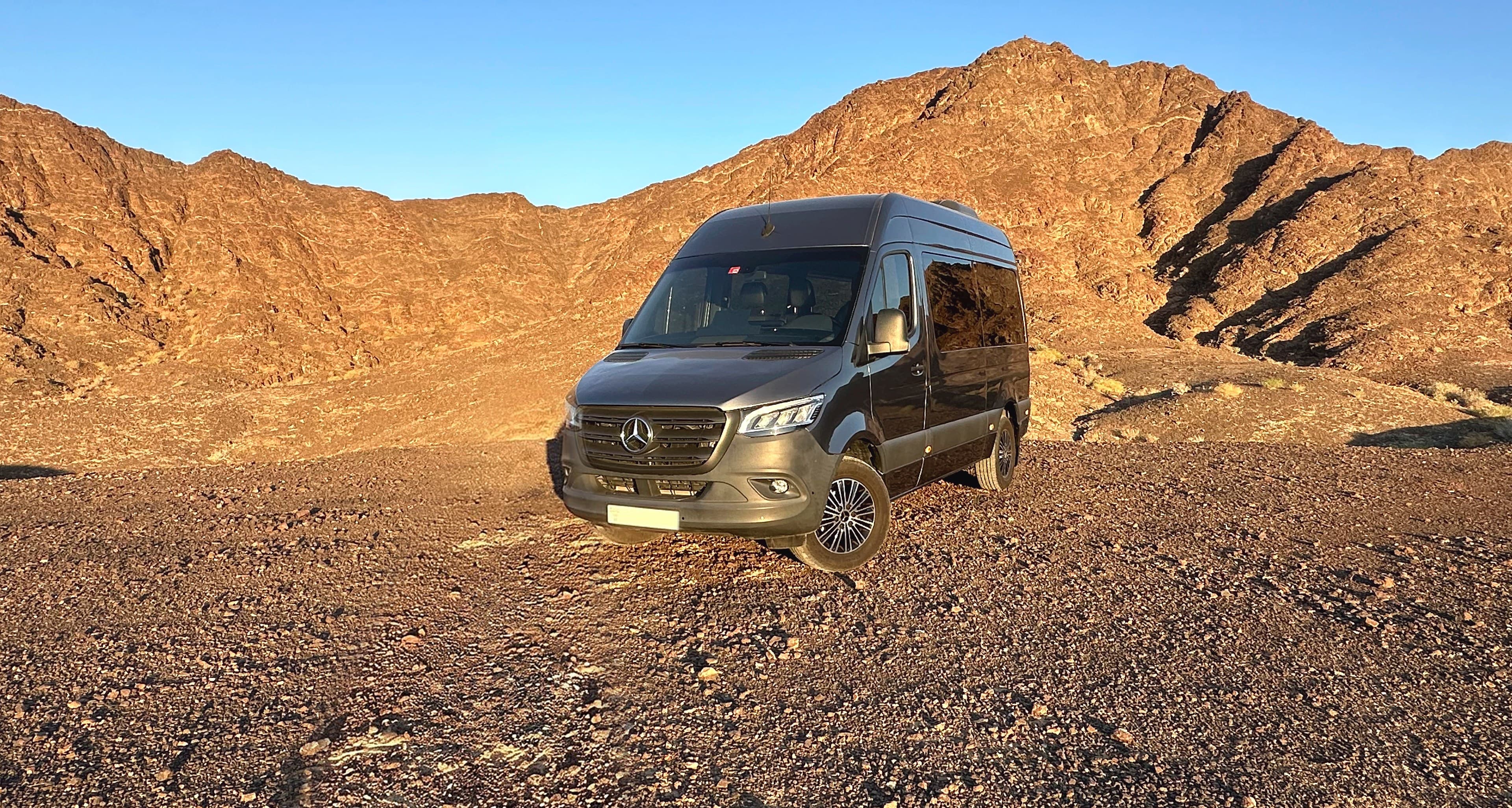 TFSL's own grey Mercedes Sprinter, high roof, parked on the Hatta road with the mountains behind it